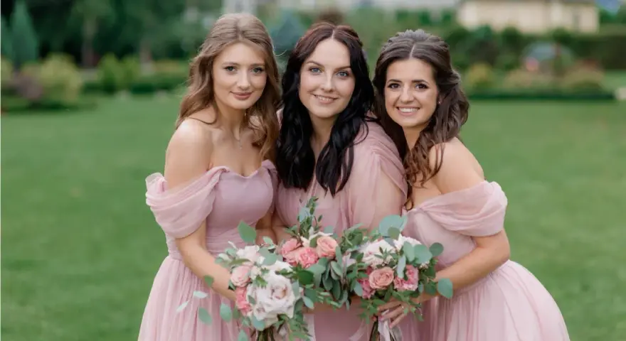 Trois demoiselles d'honneur souriantes en robes roses, tenant des bouquets de fleurs. Une belle scène pour une demande demoiselle d'honneur.