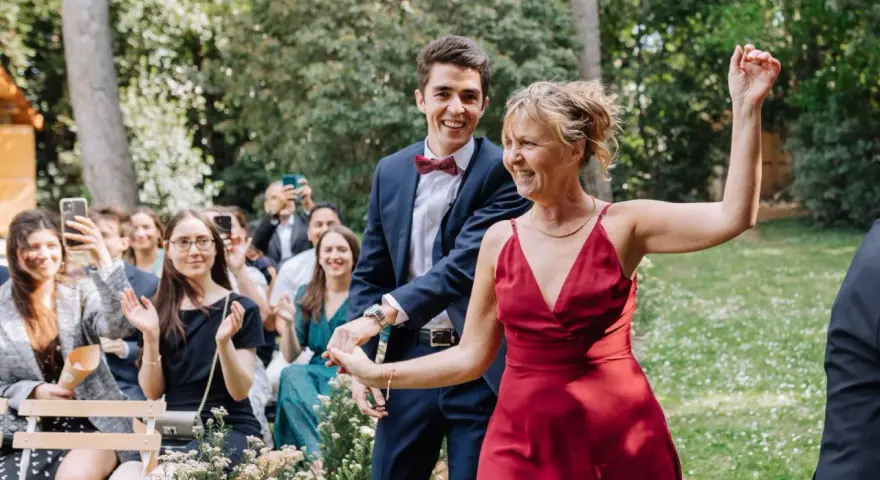 Un couple rayonnant danse lors d'un cortege mariage en plein air. La foule applaudit et filme ce moment joyeux.