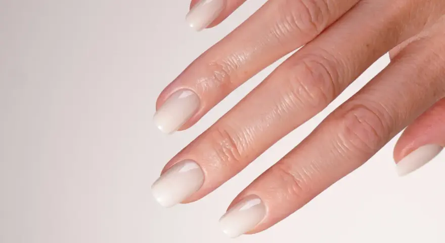 Main d'une mariée avec un french manucure spécial mariage, aux ongles laqués d'un blanc nacré, prêts pour le grand jour.