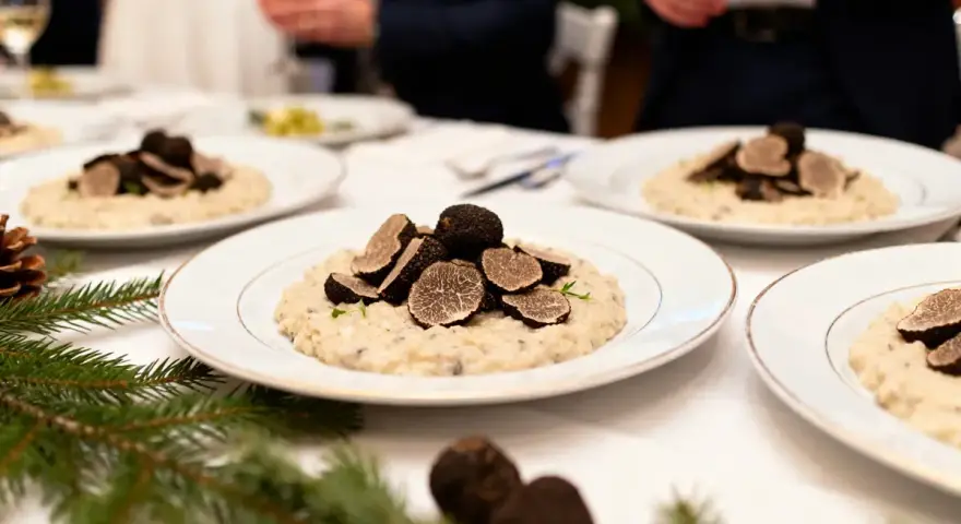 Un délicieux repas mariage hiver : des assiettes de risotto aux truffes noires, garnies de fines lamelles, sur une table dressée avec des branches de sapin.