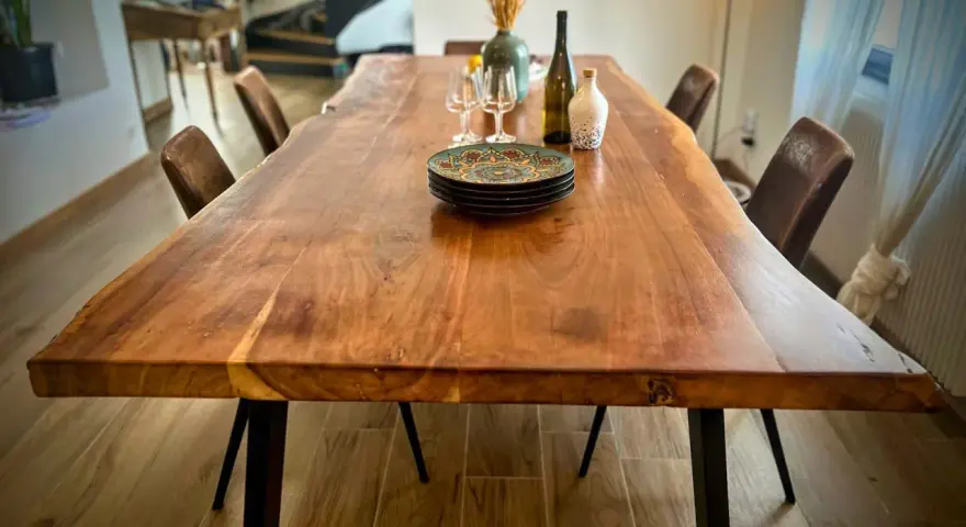 Table rectangulaire en bois massif, prête pour un repas festif dans une salle des fêtes. Assiettes décorées, verres et bouteille attendent les convives.