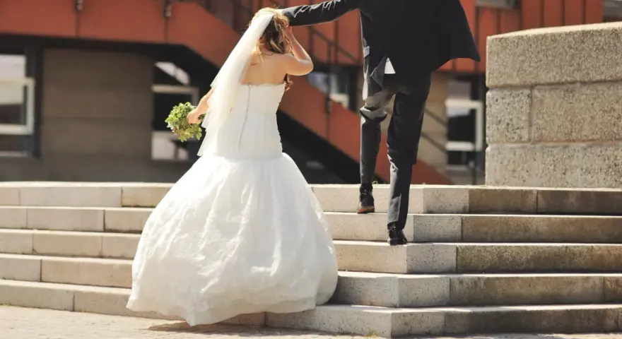 Un couple s'enfuit sur des escaliers après leur cérémonie de mariage. La mariée porte une robe blanche et un voile, tenant un bouquet.