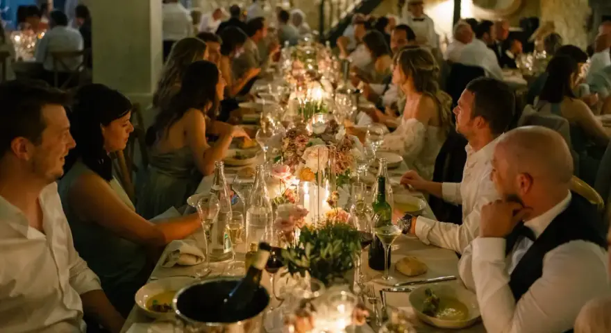 Un dîner de mariage réussi, avec une longue table dressée, des bougies, des fleurs et des invités souriants.