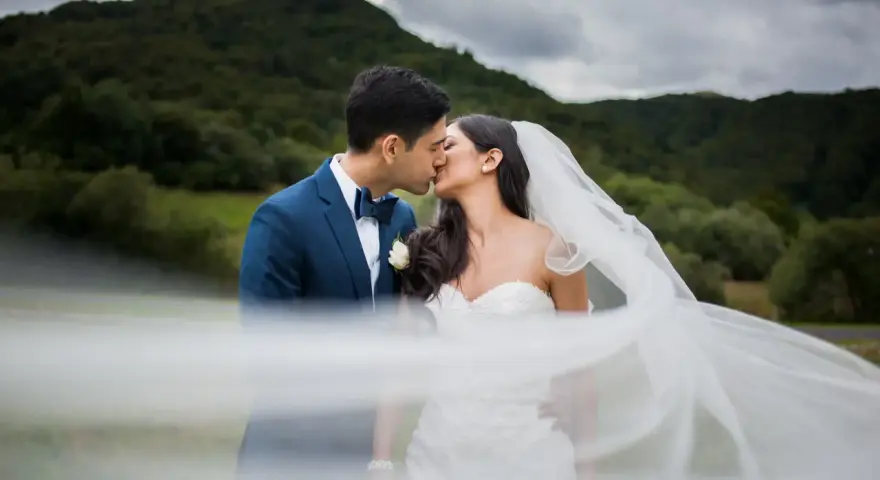 Un couple s'embrasse, le voile de la mariée flottant au vent. Une scène romantique qui donne envie de savoir comment organiser un mariage.