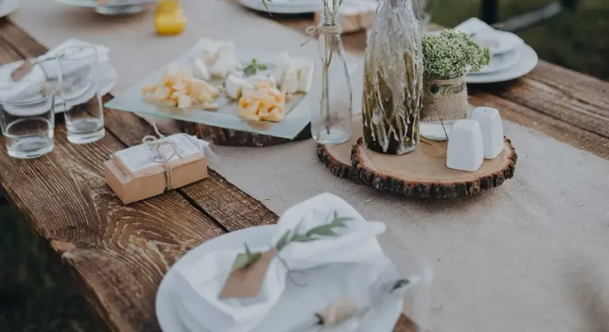 Table setting rustique pour une préparation de cérémonie laïque : assiettes, verres, plateau de fromages, cadeaux et décoration florale.