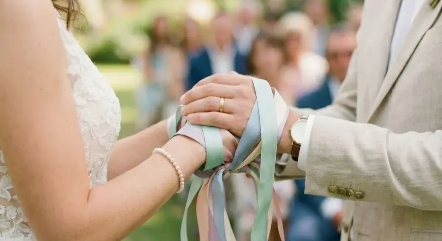 Mains jointes, rubans pastel noués, symbole d'un rituel d'union. Le couple célèbre son amour.