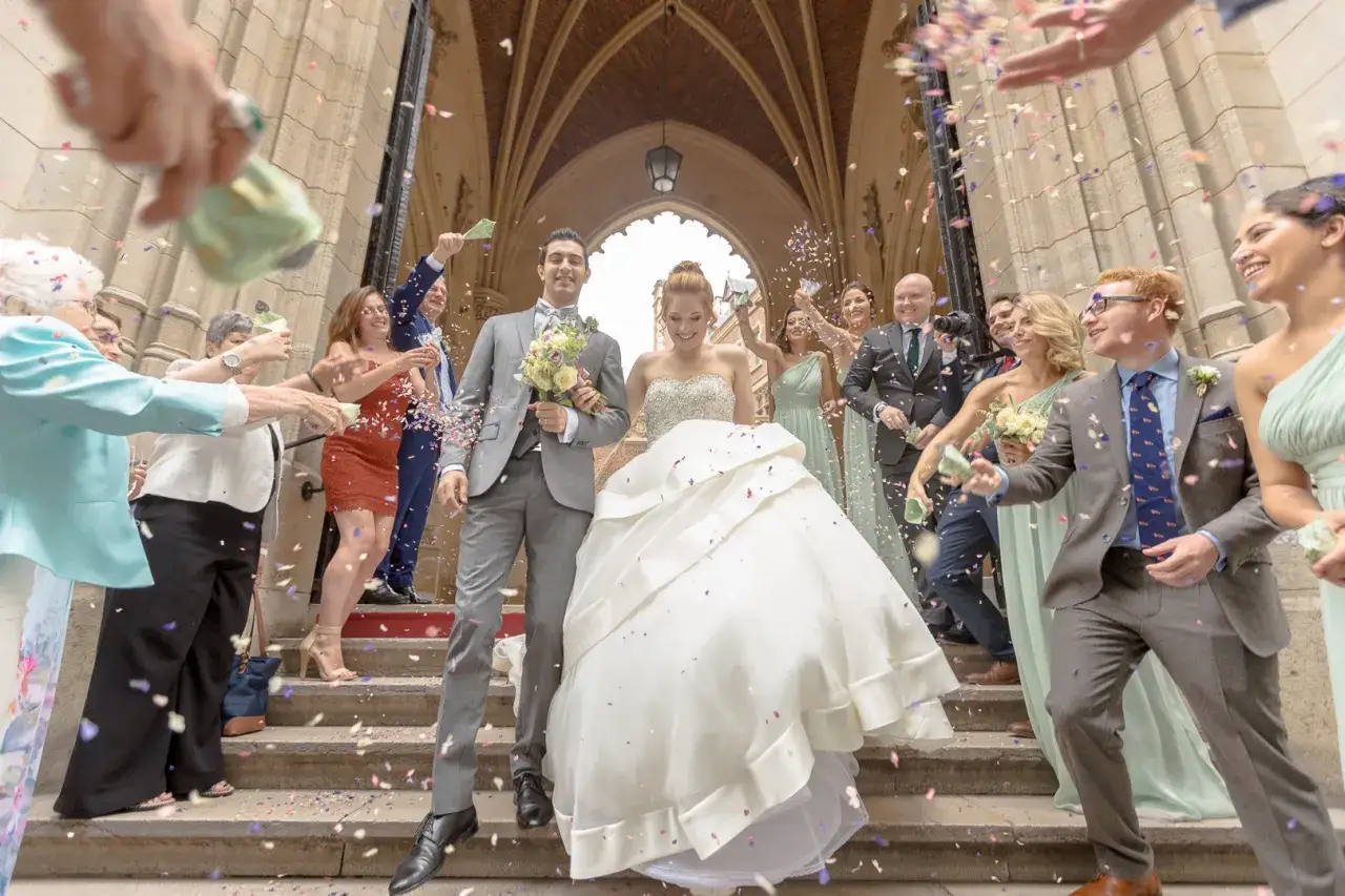 Un couple de mariés rayonnant descend les marches sous une pluie de confettis. Une scène de musique sortie mariage dynamique et joyeuse.