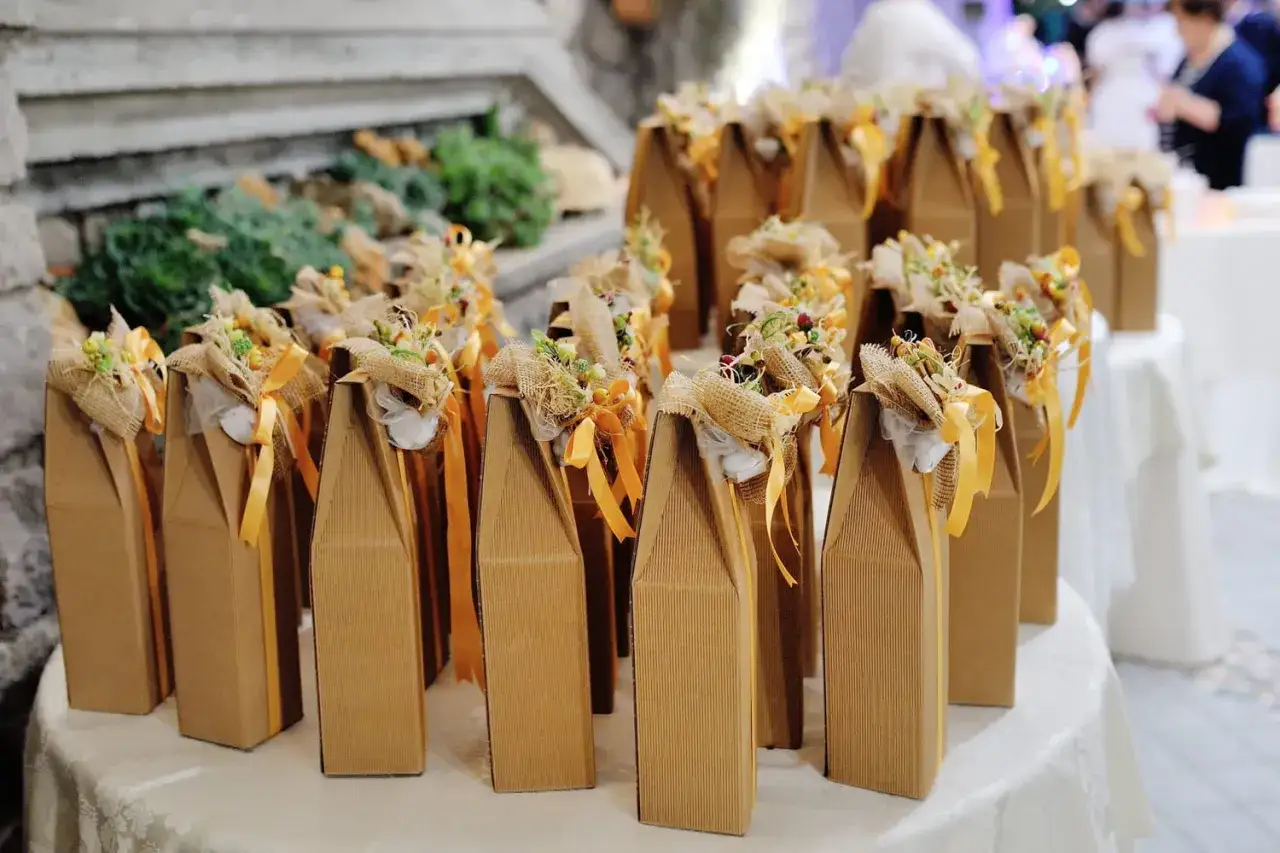 Des boîtes en carton marron, décorées de rubans et de fleurs séchées, attendent d'être offertes. Ces cadeaux invités mariage fait maison apportent une touche rustique et chaleureuse.