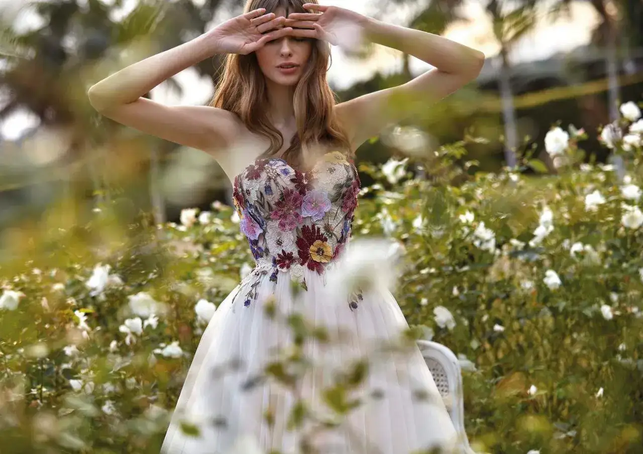 Une mariée dans un jardin fleuri, sa robe de mariée est ornée de broderies florales multicolores.