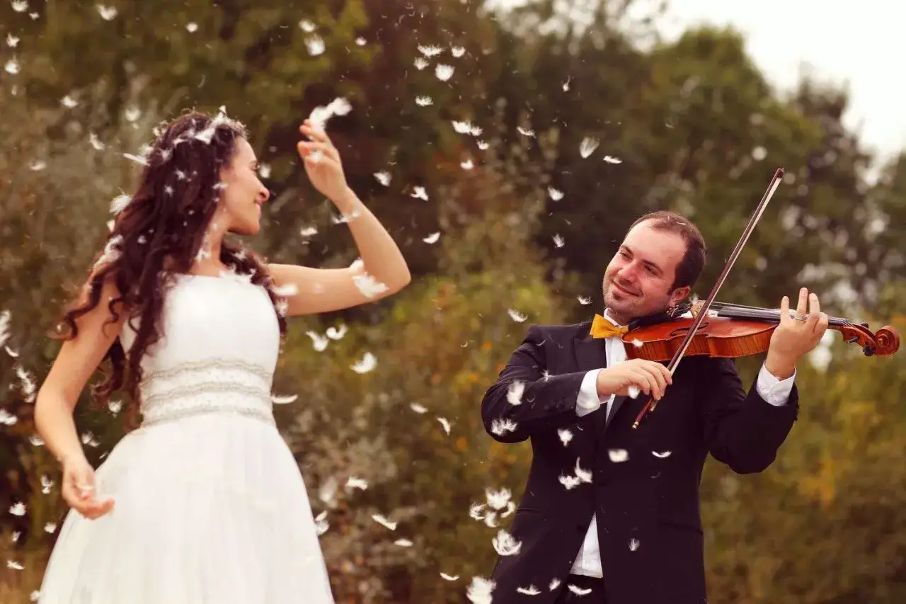 Un violoniste joue pour sa promise, une mariée en robe blanche, sous une pluie de plumes. Un mariage surprise plein de poésie.