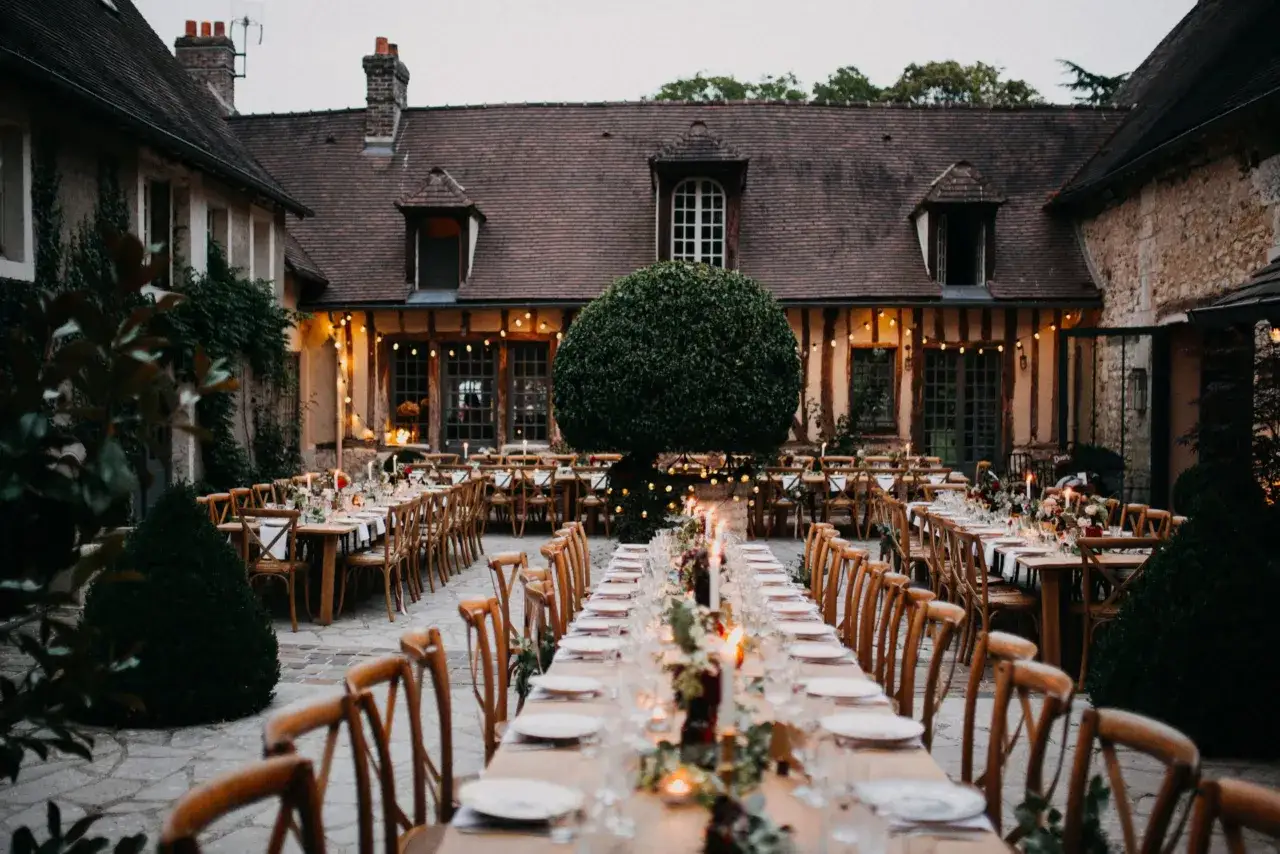Long tables set for a mariage sans dj, adorned with candles and floral arrangements, await guests in a charming courtyard.