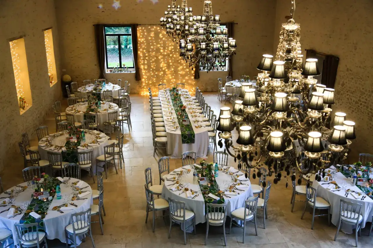 Disposition table pour 40 personnes dans une salle de réception ornée de lustres imposants et de guirlandes lumineuses.
