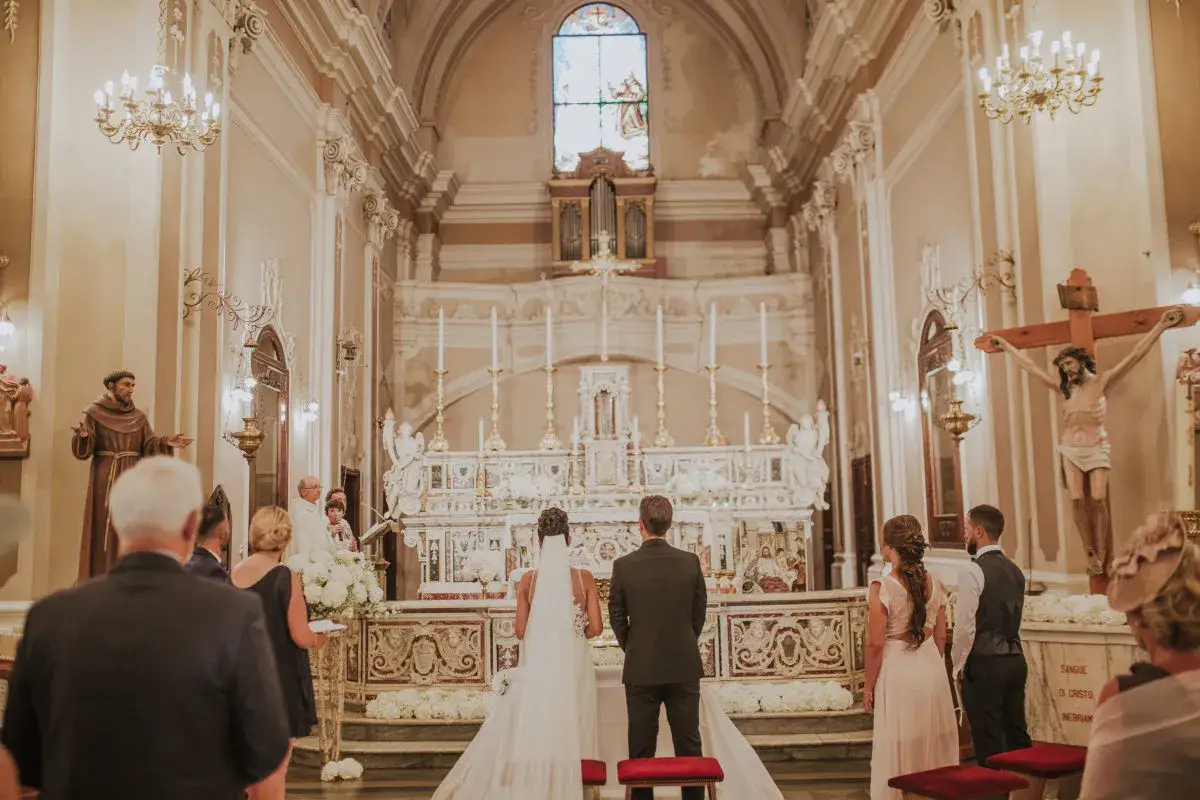 Un couple se tient devant l'autel pour son mariage religieux. L'église est ornée de fleurs et de chandeliers.