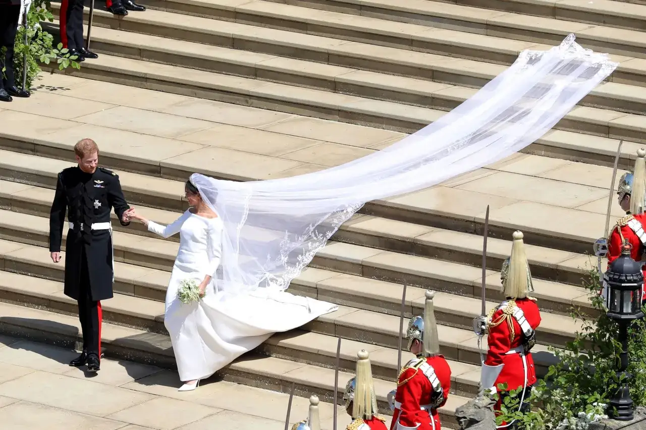 Le prince Harry tient la main de Meghan Markle, qui porte une magnifique robe de mariée et un voile spectaculaire, lors de leur mariage.