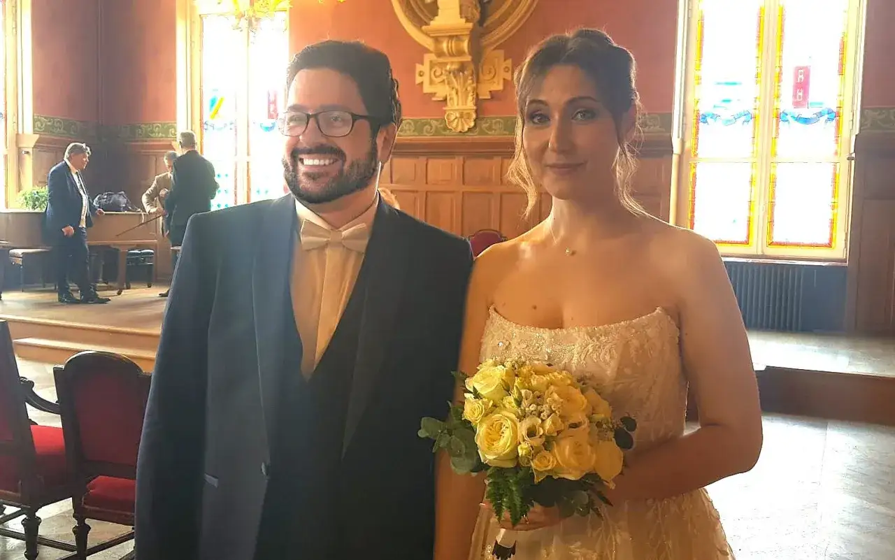 Un couple rayonnant célèbre son mariage avec un étranger. La mariée tient un bouquet de roses jaunes, le marié porte un costume élégant.