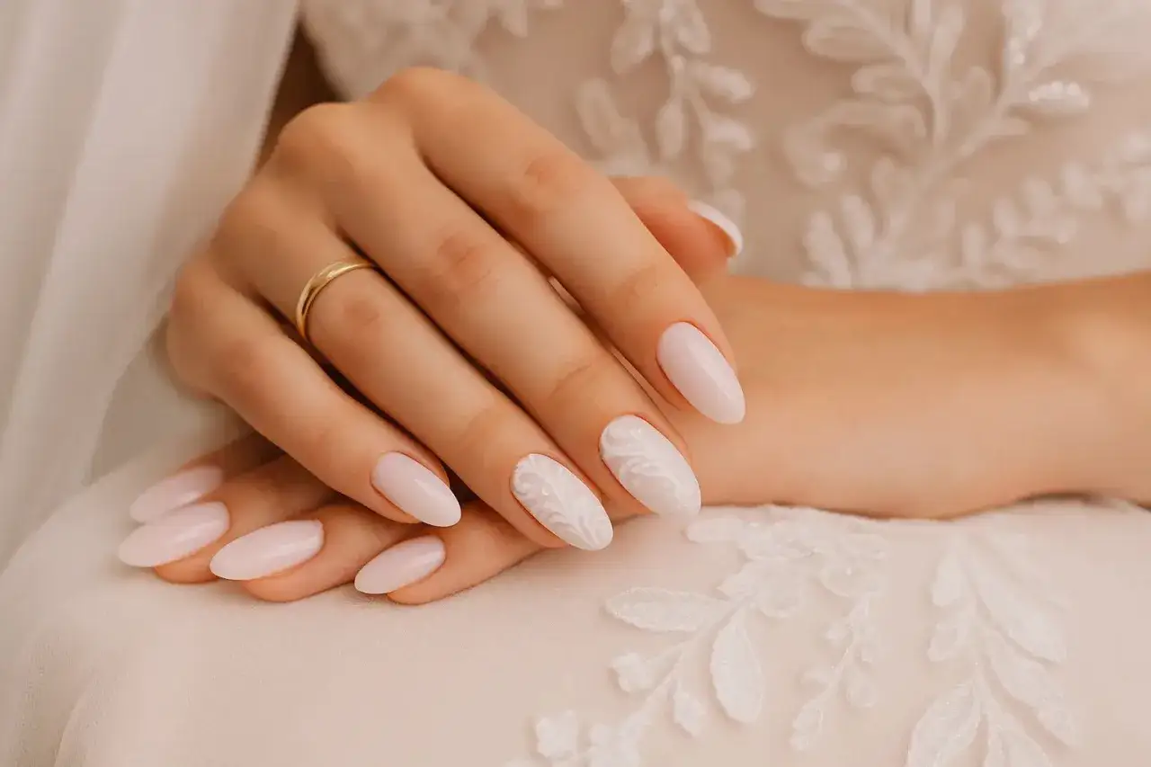 Mains d'une mariée avec des ongles tendance, ornés d'un motif floral délicat sur un fond de robe de mariée en dentelle.