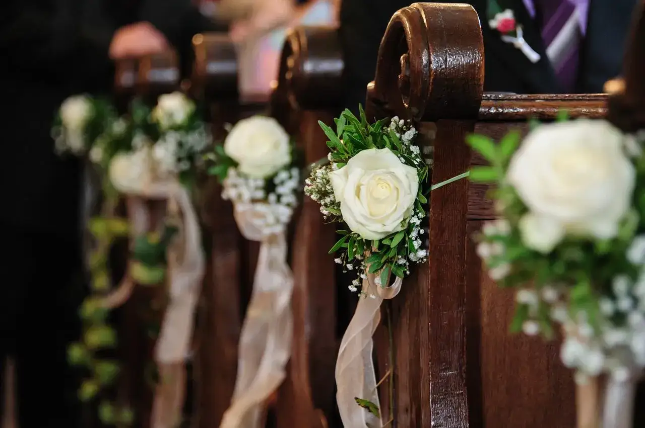 Décoration d'église pour mariage à faire soi-même : roses blanches et gypsophile ornées de rubans sur les bancs en bois.