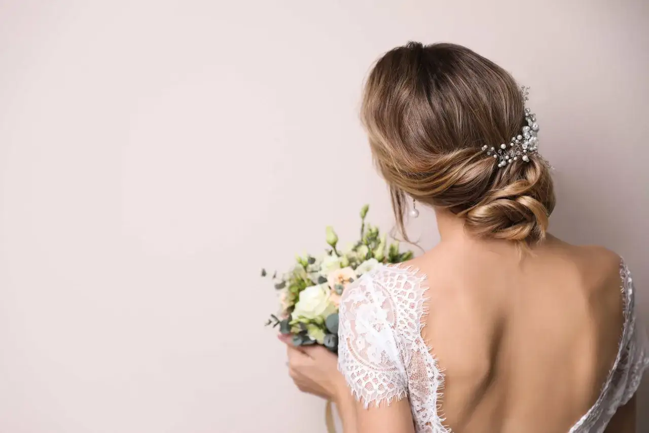 Coiffure mariage cheveux mi long, un chignon bas orné de perles et de strass, avec un bouquet de fleurs pâles.