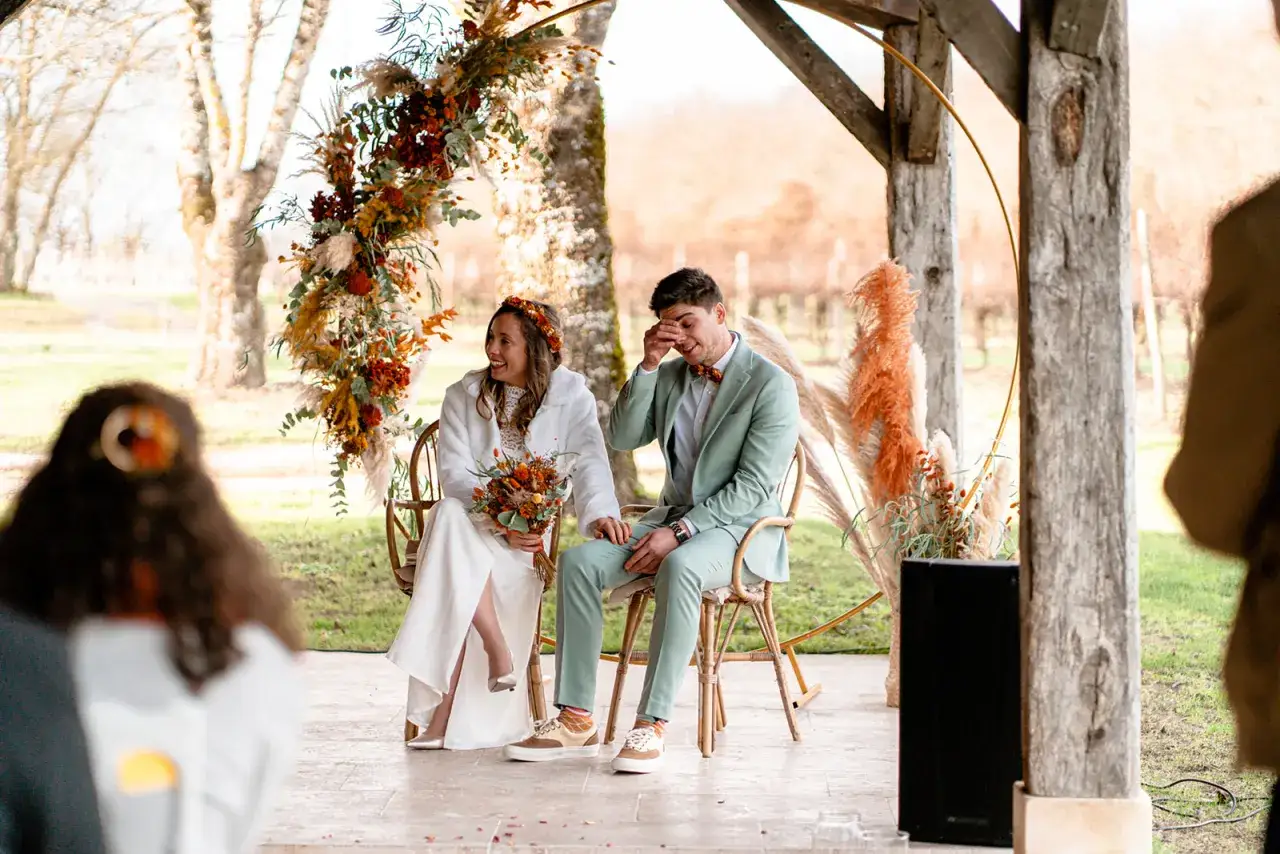Un couple rayonne lors de leur entrée pour la cérémonie laïque, entouré d'une arche florale automnale.