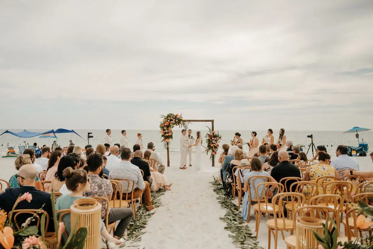 Cérémonie de mariage sur la plage, un couple échange ses vœux sous une arche fleurie. Une belle idée pour savoir où se marier à l'étranger.