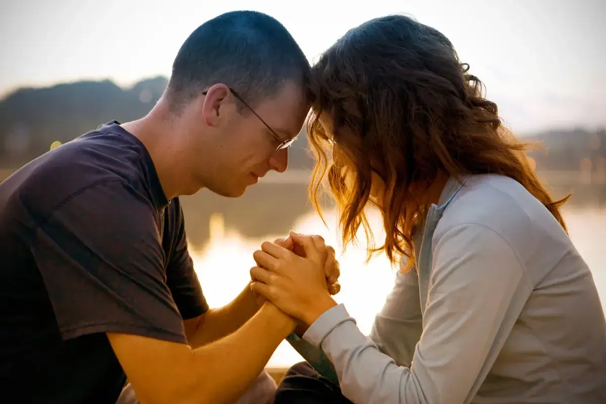 Un couple uni dans la prière des époux, front contre front, mains jointes, partageant un moment de foi et d'amour au coucher du soleil.