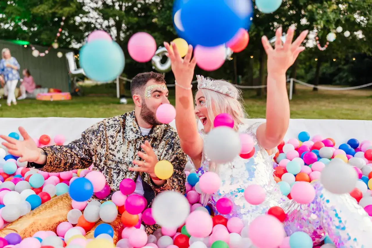 Un couple joyeux, paré de paillettes, s'amuse dans une piscine de balles colorées, une scène parfaite pour une animation mariage.