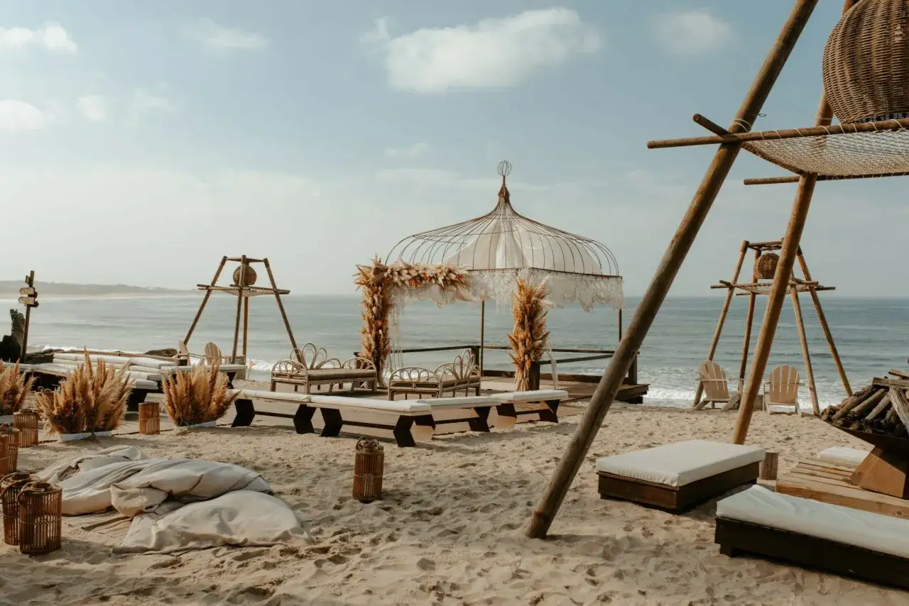 Un décor de rêve pour un mariage Portugal sur la plage, avec un dais orné de pampas et des sièges en rotin face à l'océan.