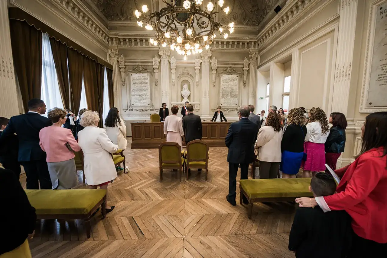 Cérémonie de mariage dans une salle ornée, avec le couple et leurs 5 témoins mariage attendant devant le bureau de l'officier d'état civil.