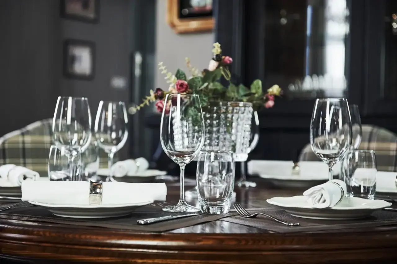 Une table dressée pour un repas, avec des verres à pied et quel côté verre à eau, des assiettes blanches et des serviettes enroulées.