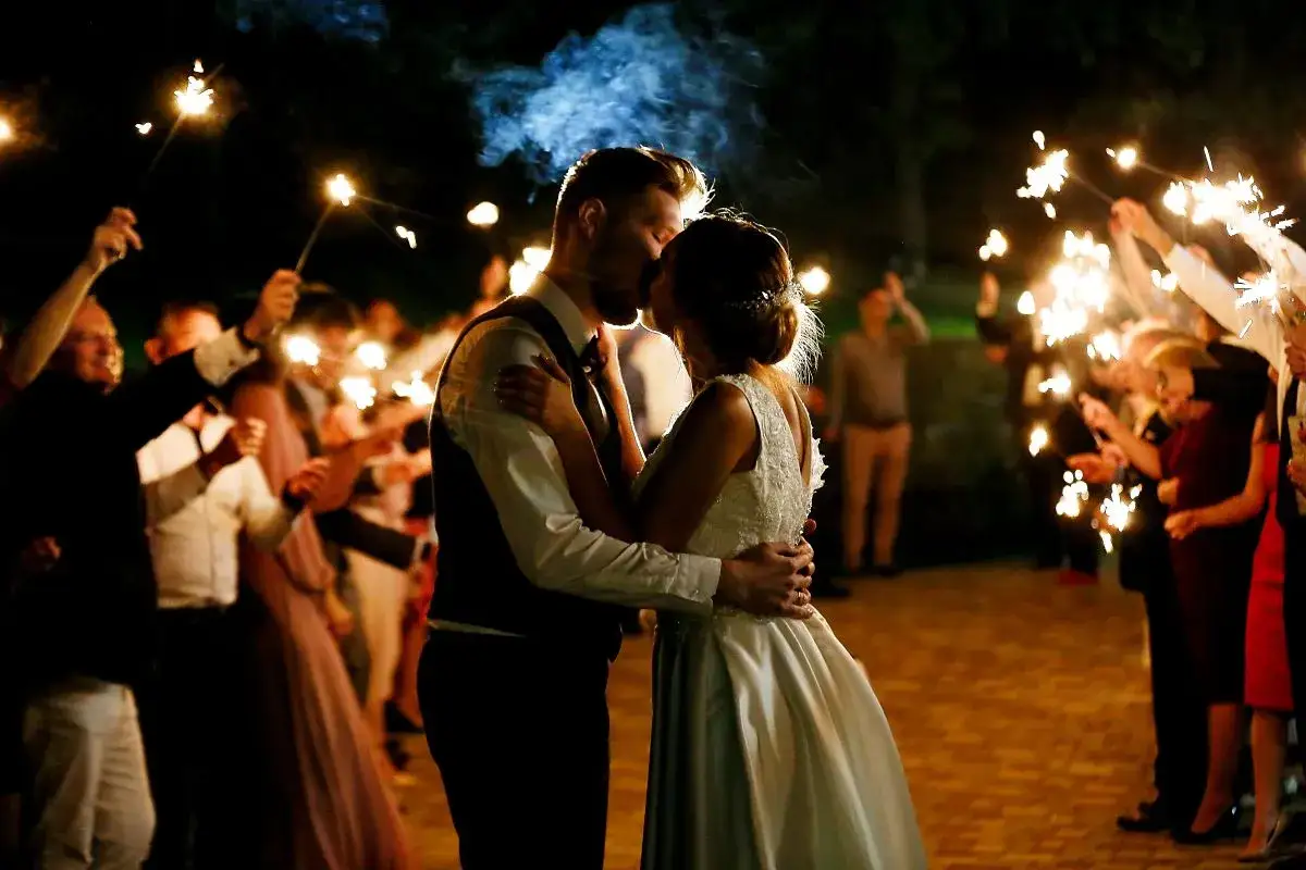 Un couple s'embrasse sous des feux de Bengale, entouré d'invités. Une belle idée d'animation mariage témoin pour un moment magique.