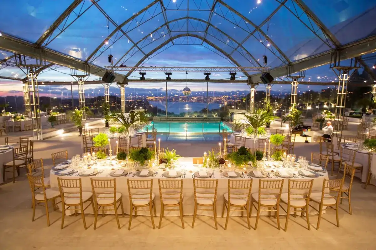 Magnifique réception de quinta mariage Portugal sous tente transparente, avec piscine illuminée et vue panoramique sur la ville au crépuscule.