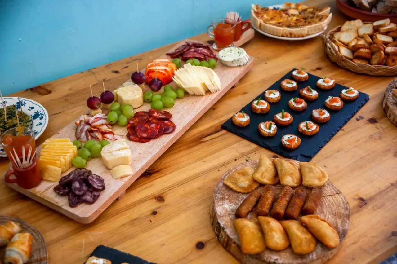 Un festin de mariage fait maison : plateau de fromages, charcuteries, raisins, mini-quiches et amuse-bouches variés sur une table en bois.