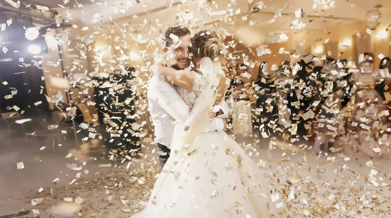 Un couple de mariés s'embrasse sous une pluie de confettis dorés. Une belle idée de ce que lancer sur les mariés pour célébrer leur union.