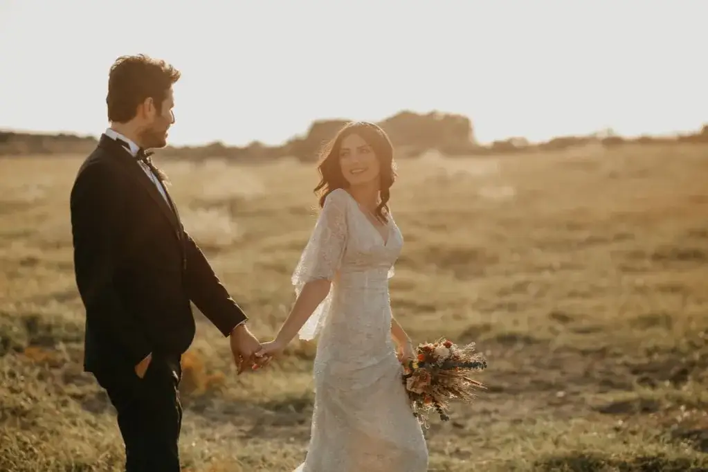 Un couple de mariés se promène main dans la main dans un champ doré, évoquant la douceur d'un exemple de vœux mariage laïque.