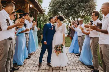 Un couple s'embrasse lors de leur petit mariage de 20 personnes. Les invités, en tenues bleues et blanches, applaudissent joyeusement.