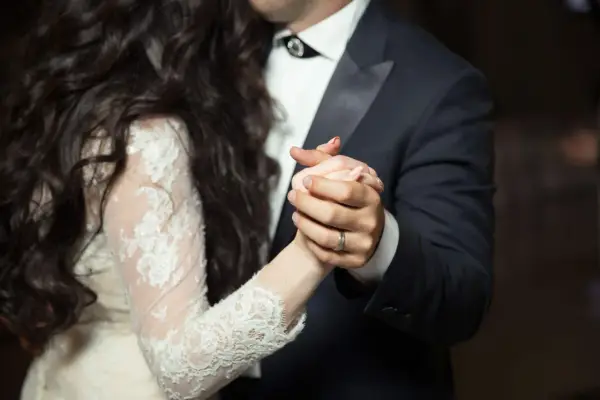 Les mains jointes d'un couple dansant une valse mariage. La mariée porte une robe en dentelle, le marié un costume sombre.