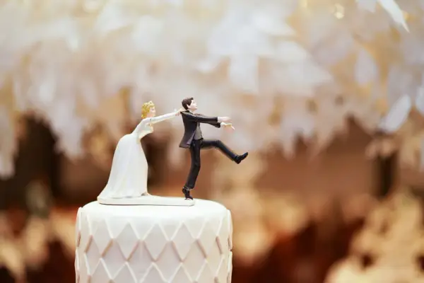 Figurines de mariés sur un gâteau. La mariée tire le marié par le revers. Un clin d'œil humoristique sur le prix d'un gâteau de mariage pour 100 personnes.