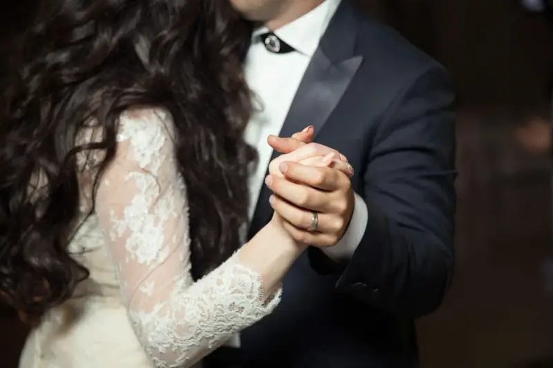 Les mains jointes d'un couple dansant une valse mariage. La mariée porte une robe en dentelle, le marié un costume sombre.