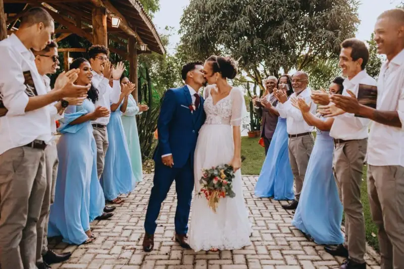 Un couple s'embrasse lors de leur petit mariage de 20 personnes. Les invités, en tenues bleues et blanches, applaudissent joyeusement.