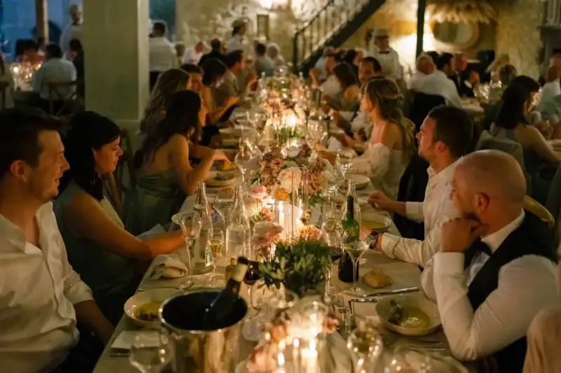 Un dîner de mariage réussi, avec une longue table dressée, des bougies, des fleurs et des invités souriants.